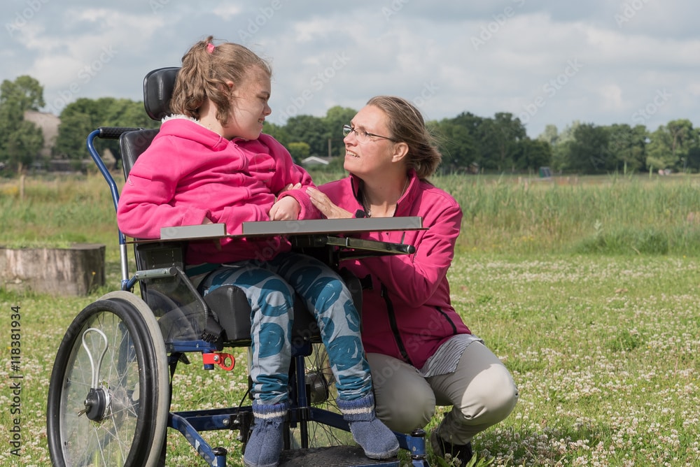 Special needs child in wheelchair next to a kneeling woman